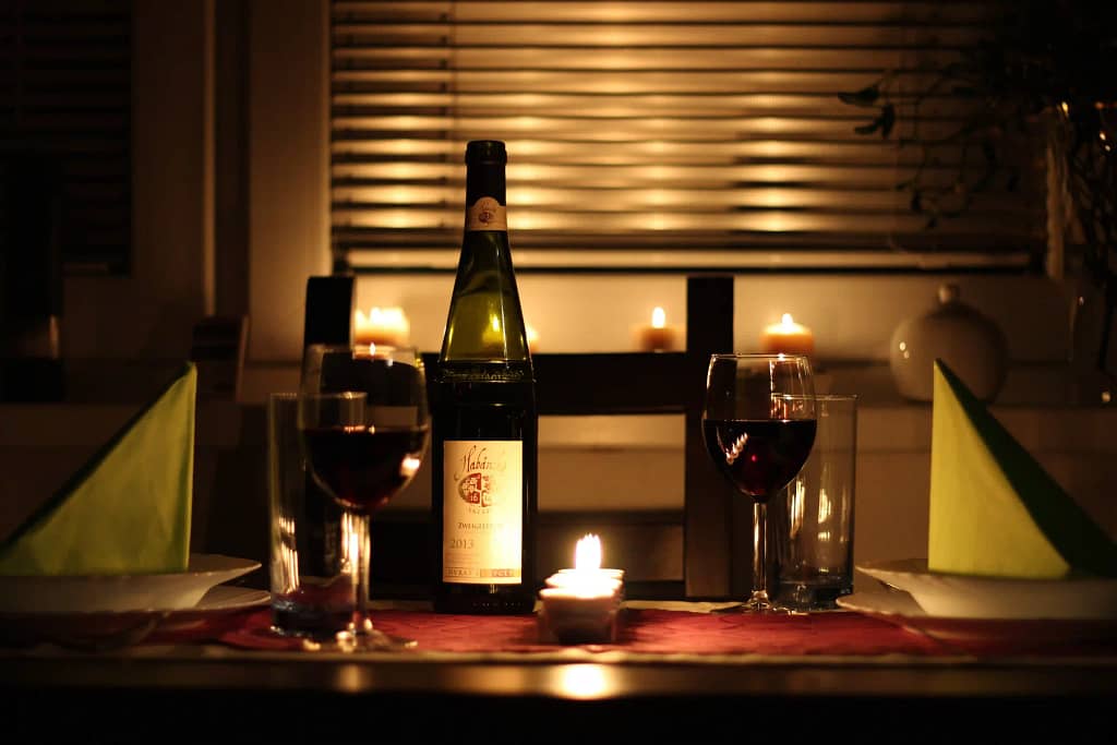 A table with a bottle of wine, glasses, and candles set for a date night. 