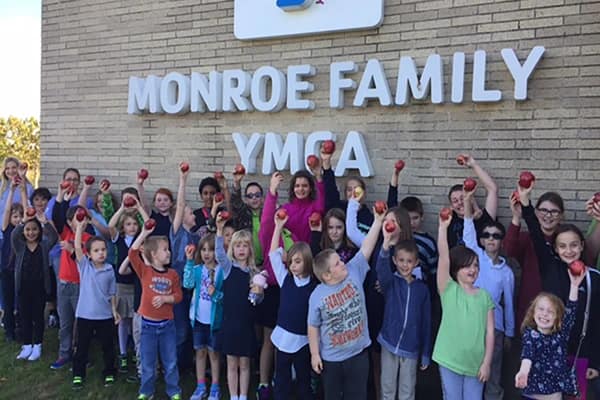 Kids and adults holding red Apples high and taking a photo at the Monroe Family YMCA