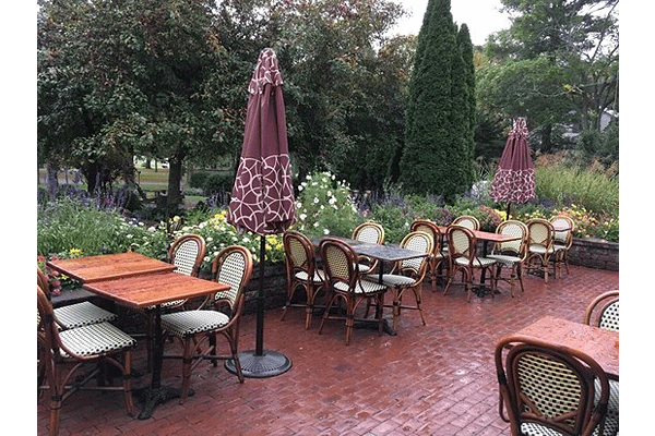 tables and chairs set outdoors with trees and flowers.