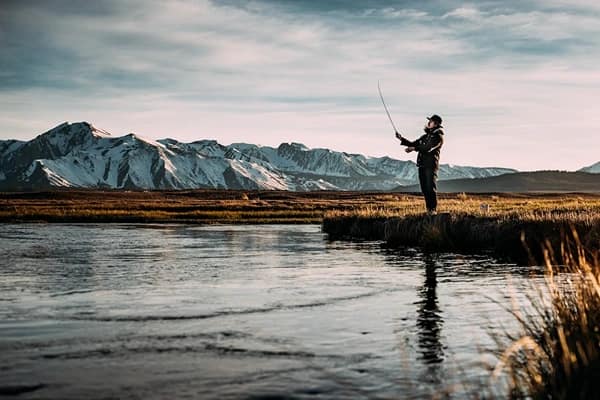 a man fishing in the river with mountains in view