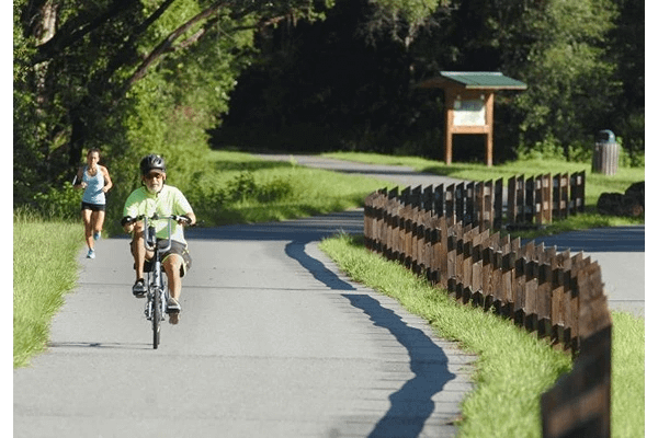 A man riding a bicycle along a smooth trail with a woman jogging behind him.