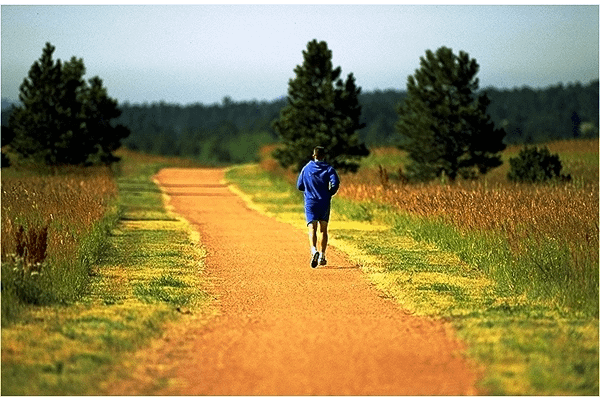 A man jogging on a trail with trees around and in the distance