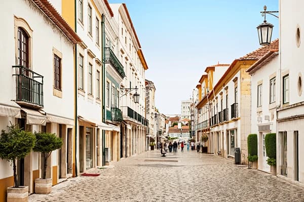 A street with off white buildings and green accents with people walking at day time.