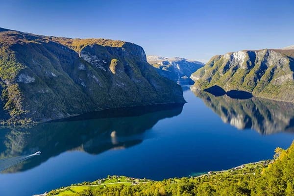 Fjord Cruise - A boat moving on the large  still waters with huge mountains by the sides and green vegetations.