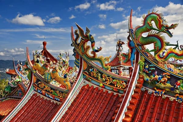 Colourful dragon sculptures on red roofs under blue skies with some clouds