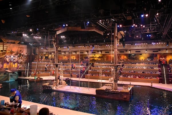 A stage surrounded by water and lit with many stage lights with people sitting around and watching the show.