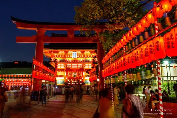 A Japanese street at night lit with red lanterns and people walking around