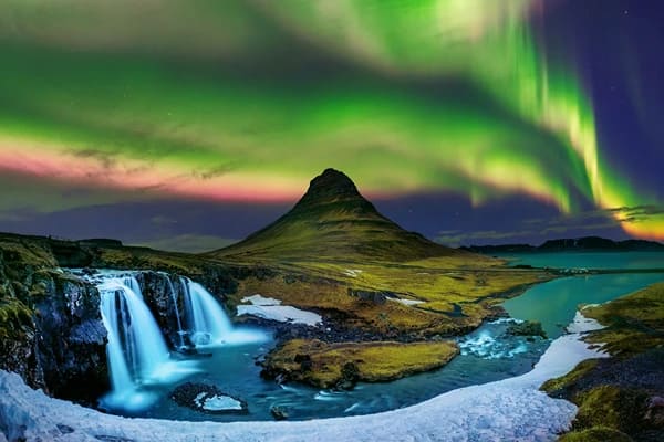 Colourful green lights in the sky with mountains and waterfalls under 