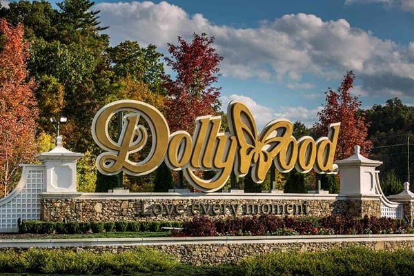 A huge sign that says "Dollywood" surrounded by beautiful trees and grasses