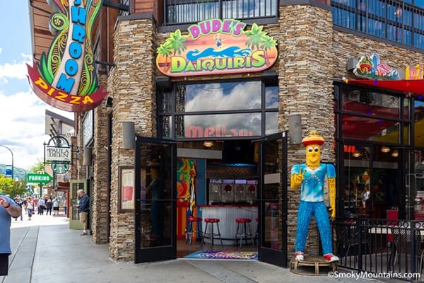 A building with open doors in daylight with a colourful mascot standing in front of it and Dude Daiquiris sign over it.