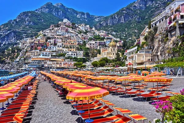 A beach shore with many colourful gazebos surrounded by tall mountains 