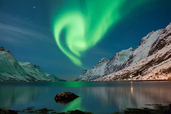 Beautiful green lights (Northern Lights) in the night sky surrounded by tall mountains 