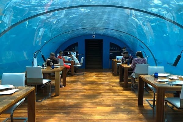 An underwater restaurant with tables set and tourists operating their mobile devices