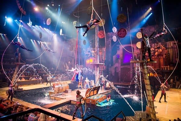 A stage surrounded by water with people performing air acrobatics and an audience watching.