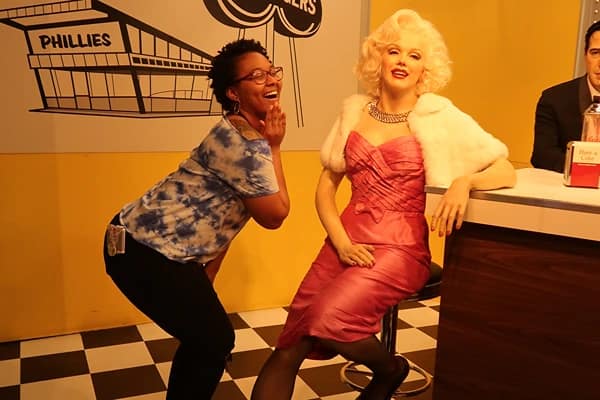 A woman posing in front of a wax sculpture of Marilyn Monroe