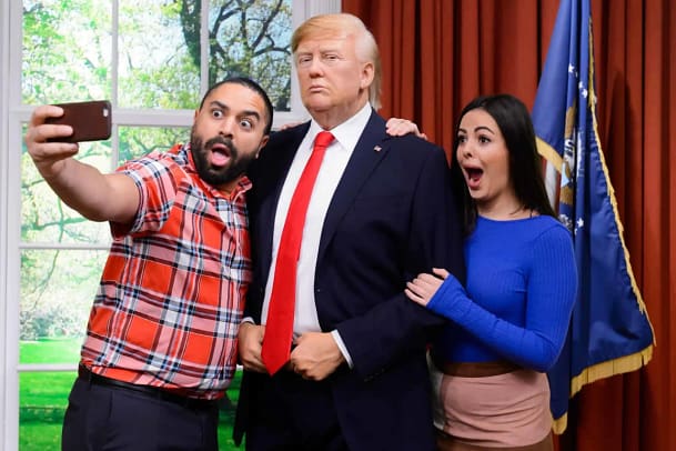 Two people taking a photo with a sculpture of Donald Trump at Madame Tussauds