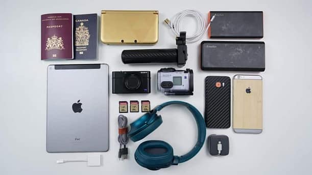 A collection of traveling items for men including a wallet, smartphones, passports, SD cards, headset, chargers and power banks