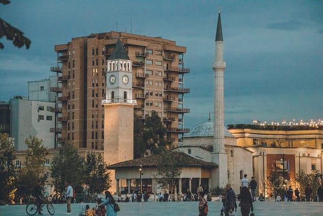 people walking pass a tall clock tower in one of the memorable places to visit in Tirana, Albania.