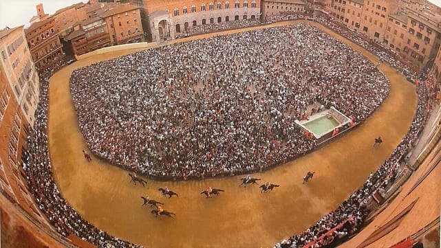 An aerial view of a very large crowd with horses running around in circles