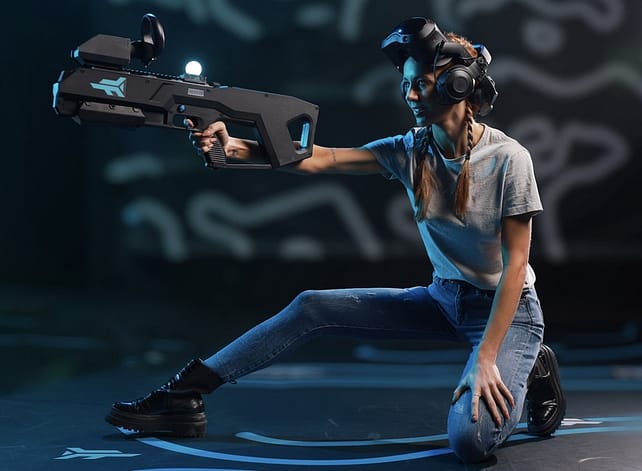 a lady with a VR headset, and an electric gun in a large room