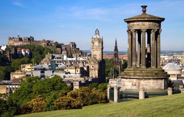 A photograph of Edinburgh showing a tall architectural buildings surrounded by green land and trees
