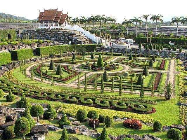 Nong Nooch Tropical Botanical Garden, Thailand. A well-organized area with trimmed flowers of different shapes, and tall palm trees in the background