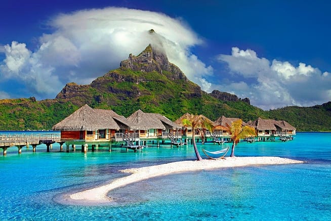 A scenic picture of little huts floating on a river in  a beach in Bora Bora