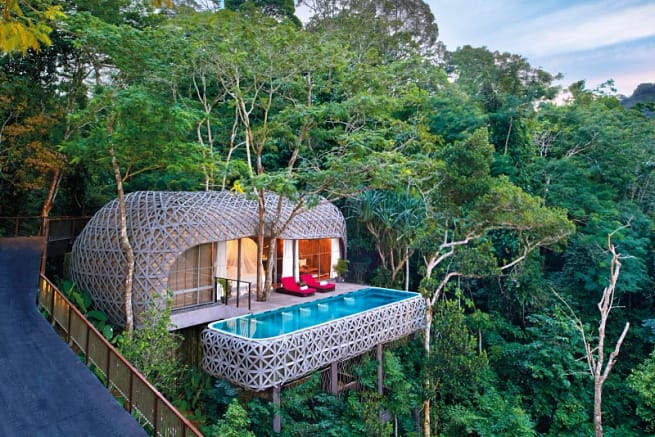 A tree house with a swimming pool and a sit-out with red resting chairs
