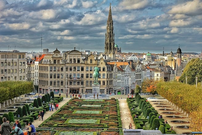 A beautiful photograph of a city in Brussels, Europe, showing tall buildings and beautiful well-cut flowers with a statue in the center