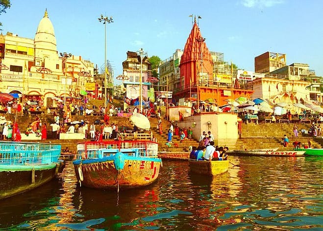 A colourful scene in Varanasi, India with yellow painted buildings, boats and tourists wearing multi-colored wears