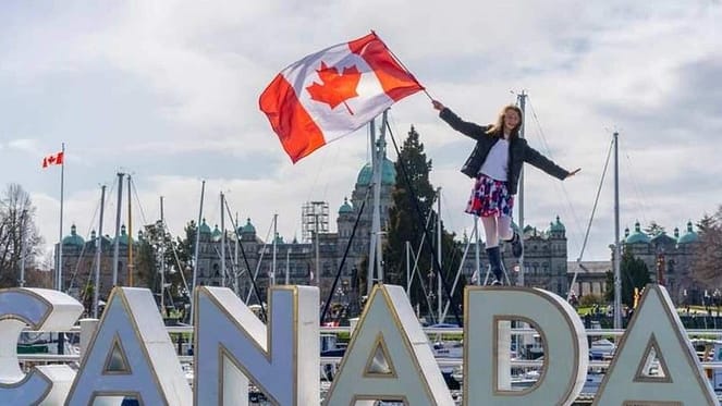 A lady holding the Canadian flag and standing on a letter statue of Canada