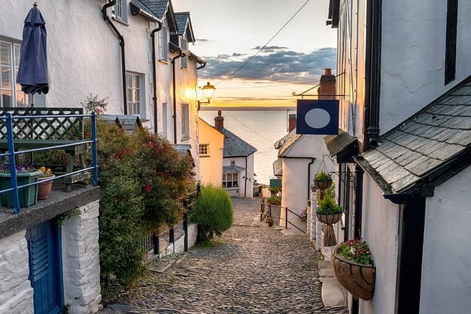 A beautiful street in Devon with ash colour painted houses, flowers and a sea casted with yellow sunset