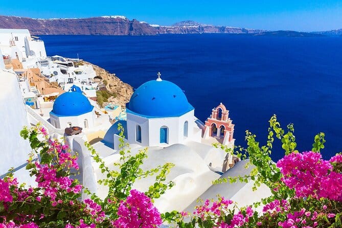 A scenic view of Athens shoeing clear blue waters, white houses with blue roofs, and colourful flowers