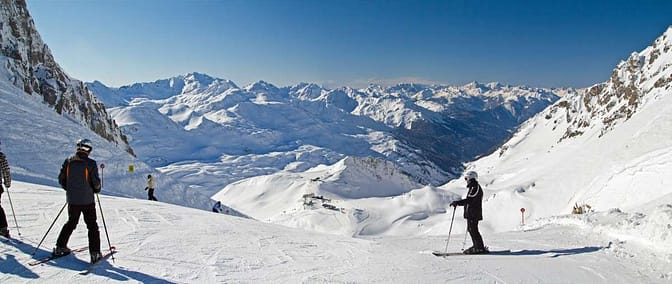 A group of people skiing in a large snow covered area with mountains surrounding them