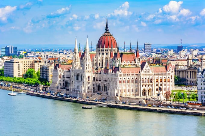 An aerial view of a city in Budapest with huge architectural buildings, skyscrapers, a sea with a few boats and tourists