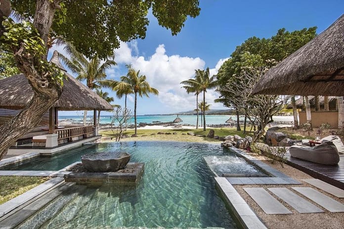 Shanti Maurice Beach Resort in Mauritius with two wooden huts and a swimming pool in the middle, surrounded by tall palm trees