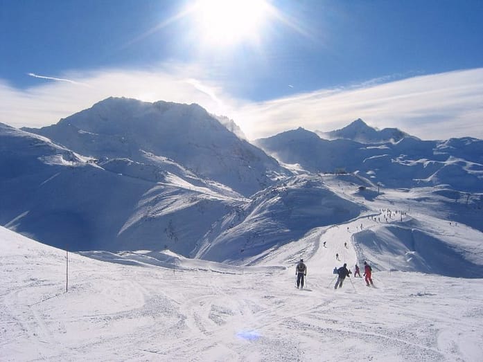 A group of people skiing in a large snow covered area with mountains surrounding them
