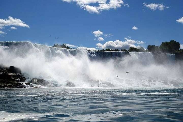 Niagara Falls, in North America with birds flying over the water and a clear blue sky above it.