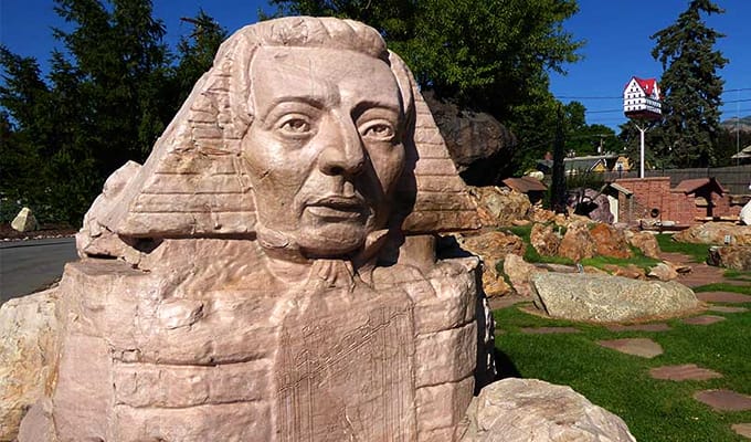 A huge sculpture of a man's head, with trees and pieces of rocks in the background