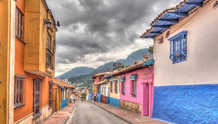 A street in Colombia with colourful houses and a rainy cloud surrounded by mountains.