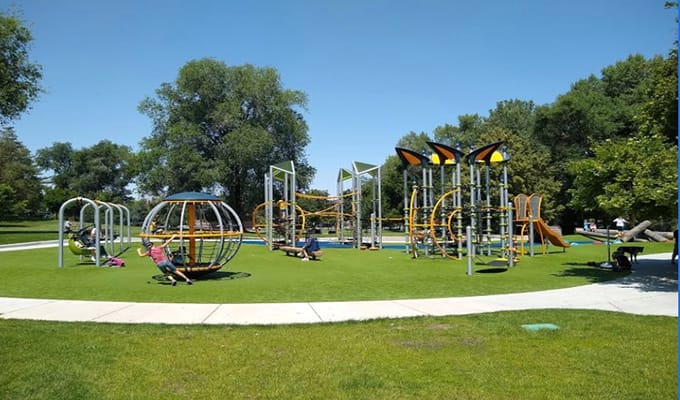 A playground park surrounded by tress with kids playing and having fun with different equipments