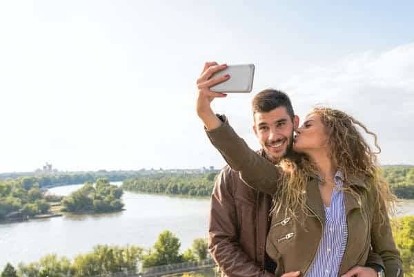 A couple taking a selfie together with a large body of water and green area behind them.
