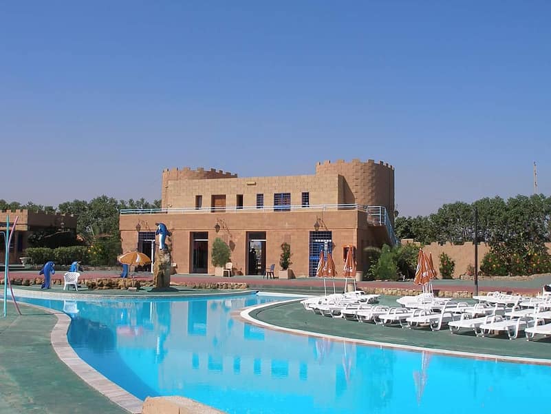 a brown building in front of a pool under a blue sky