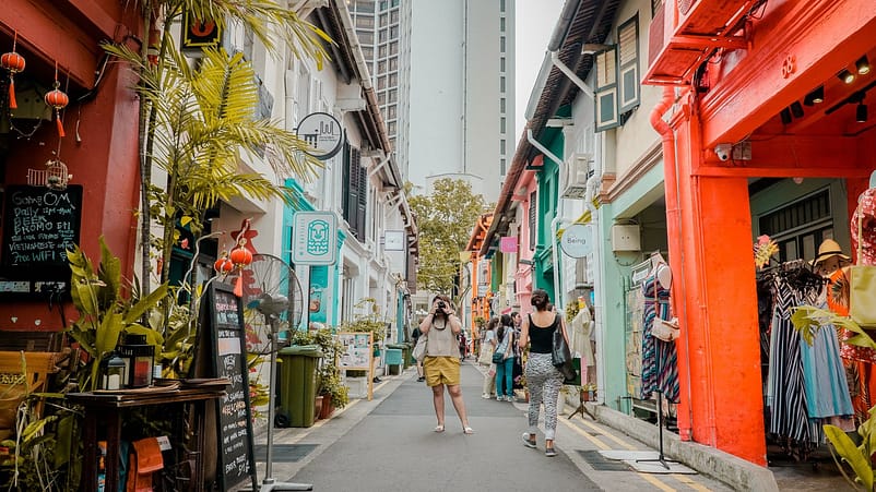 A very colourful and vibrant street with shops and businesses while passer-by's take photos 