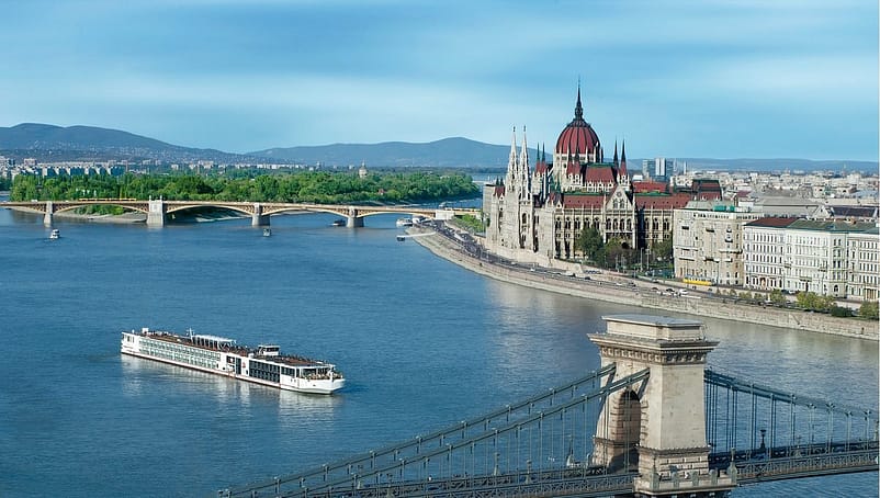 A large white cruise ship on the Danube River surrounded by a large cities and bridges