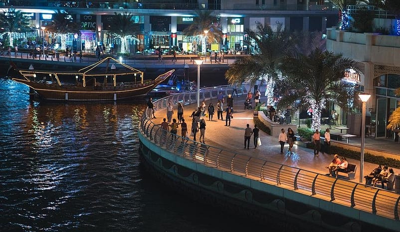 A night scene in Dubai with people walking in a large mall facing a river/large pool 