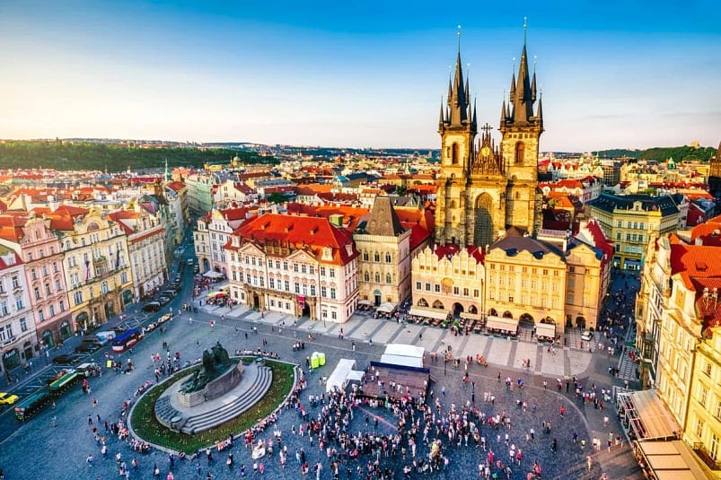 An aerial view of a large open space with tall buildings surrounding people walking around in Prague, Czech Republic