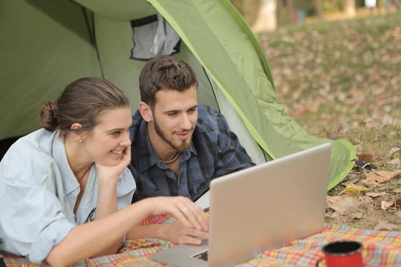 A white couple under a tent smiling as they use their computer together