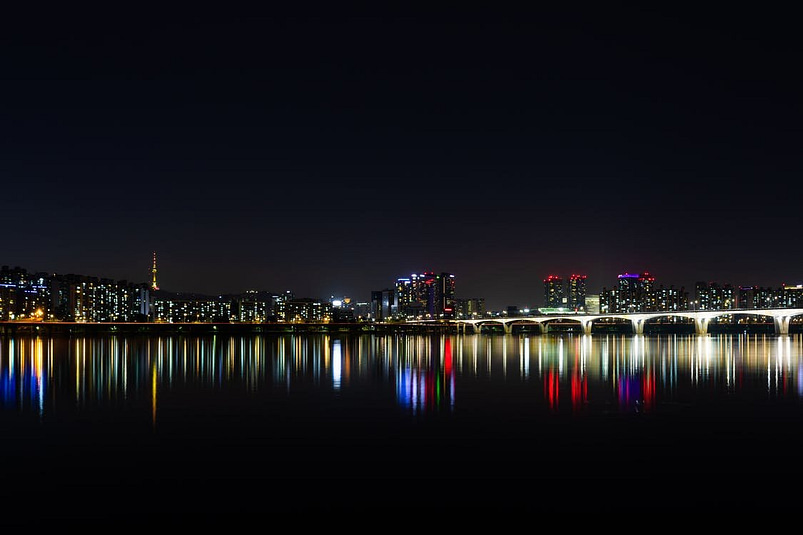 A city in South Korea at night with bright coloured lights and a dark body of water