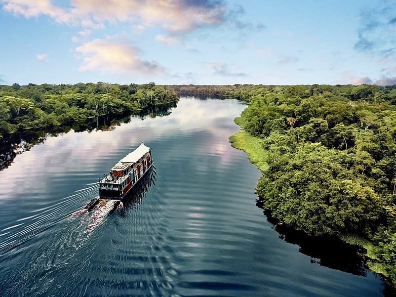A large cruise ship passing through the Amazon River, surrounded by a vast expanse of green land.